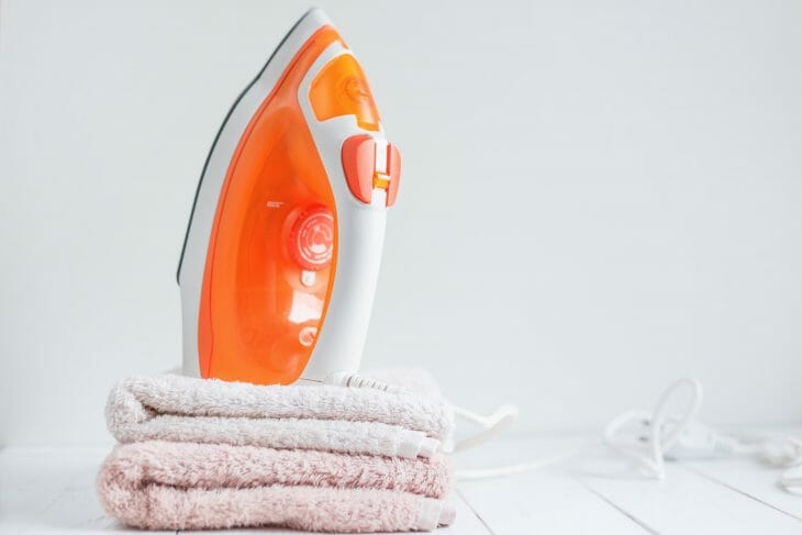 Оранжевый утюг стоит на полотенцах